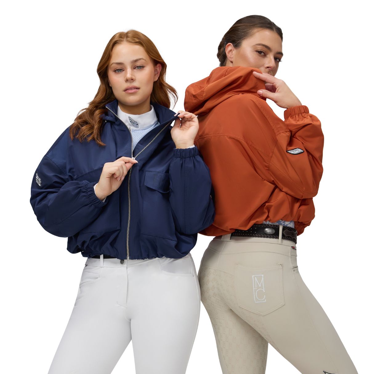 Two women wearing horse riding competition breeches, one with a navy casual jacket and the other wearing an orange casual jacket