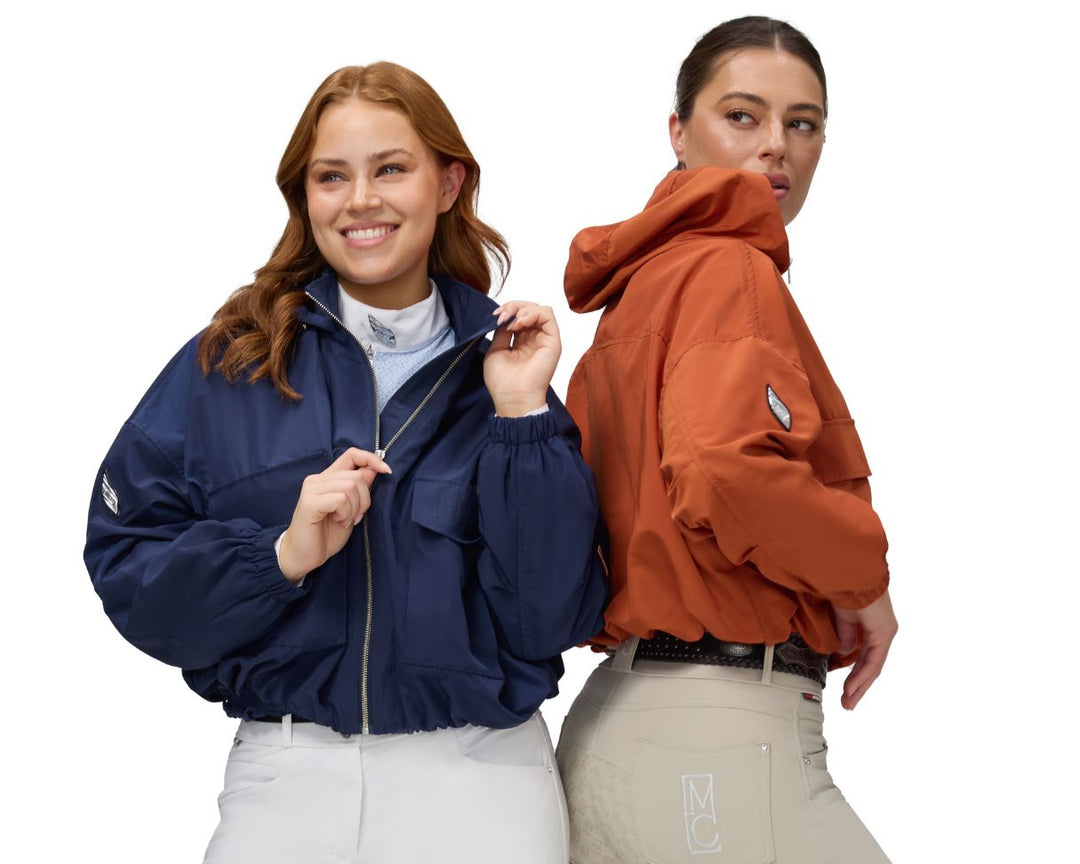 Two women wearing jackets and equestrian riding breeches on a white background