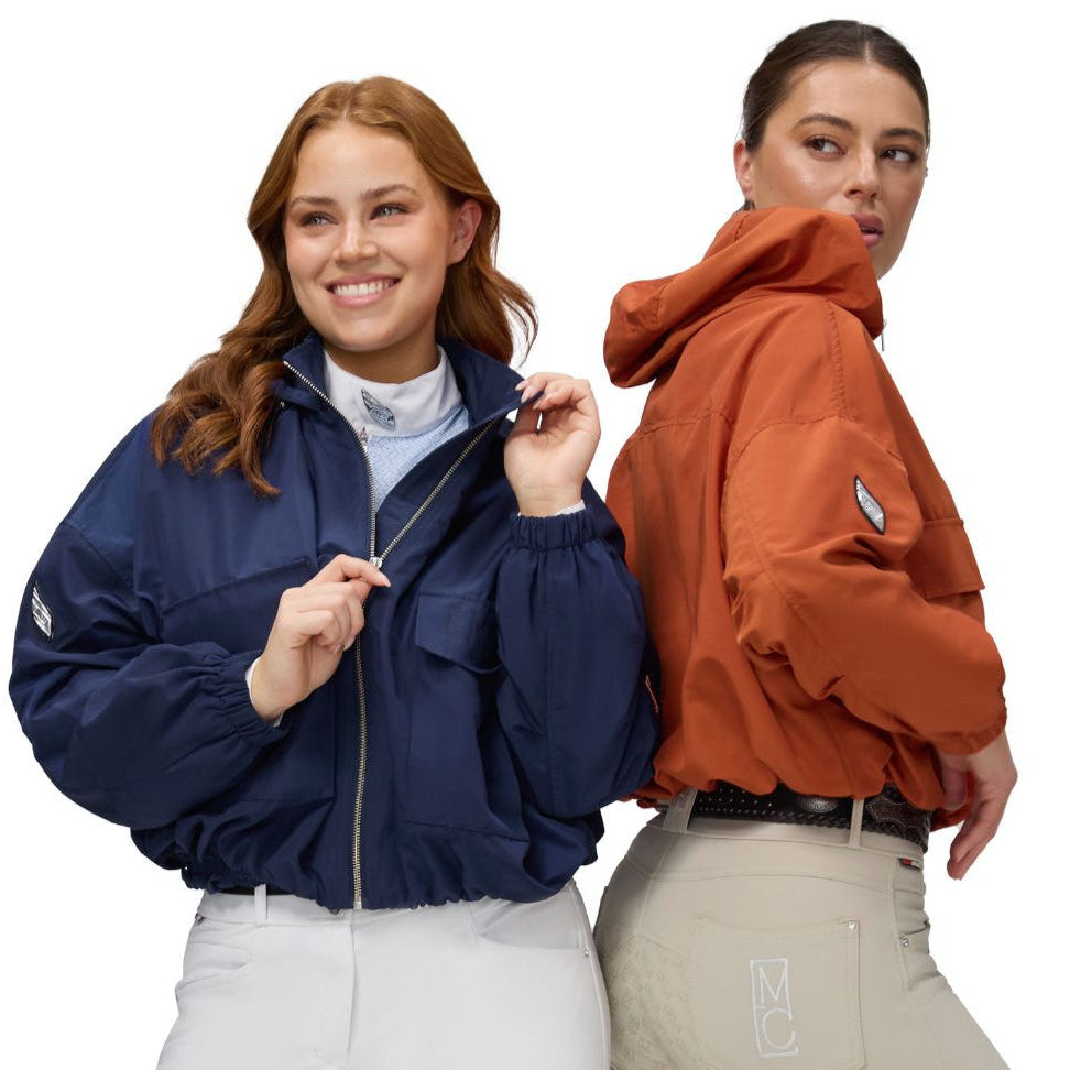 Two women wearing jackets and equestrian riding breeches on a white background